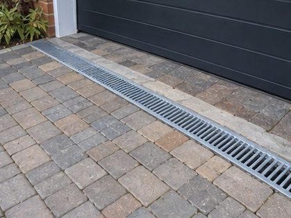 A grated channel drain set into block paving across the threshold of a garage