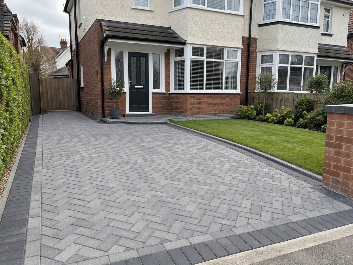A grey herringbone block paved driveway running up to a semi detached house, with a lawn down one side