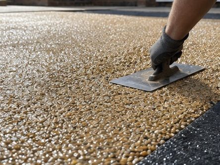 Resin bound gravel being trowelled out, the loose stone ahead of the float and the finished surface behind it