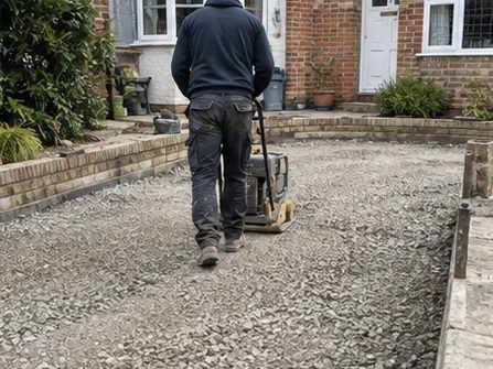 A groundworker running a plate compactor over crushed stone between the garden walls